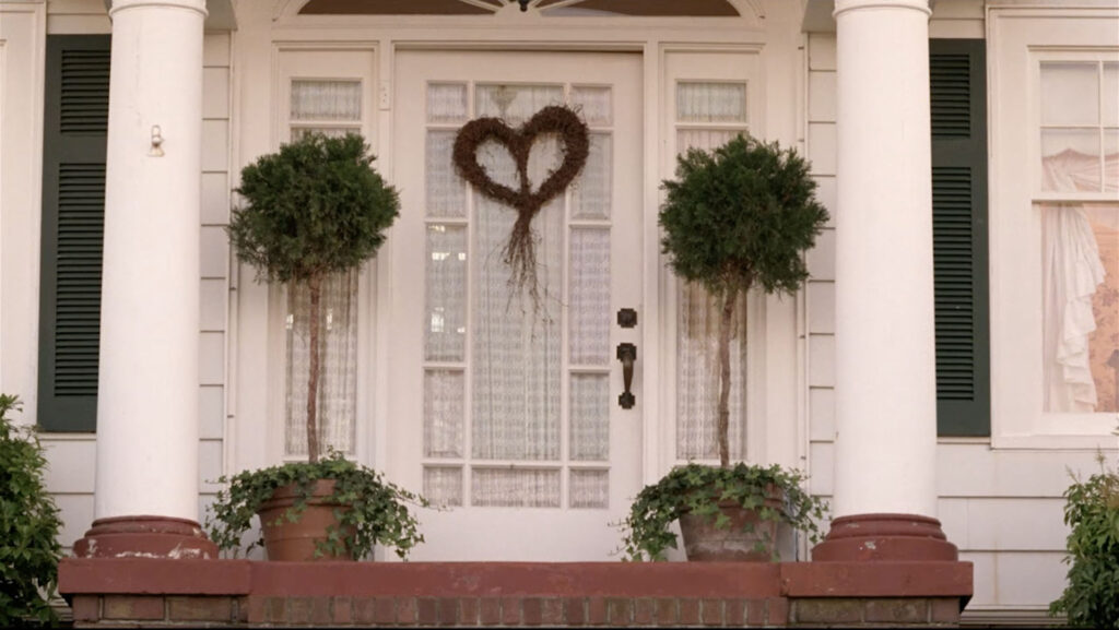 Heart-shaped wreath on the front of a white house flanked by trees