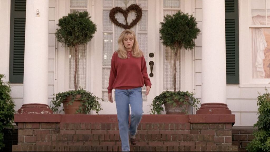 Laura Palmer walking down stairs with the heart-shaped wreath behind her hanging on the front door.