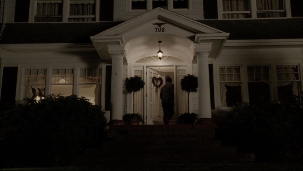 Leland Palmer entering the front door of a white house on a hill at night.