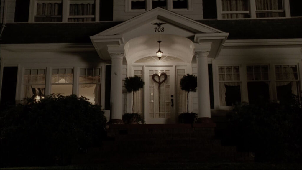 Front door of a white house on a hill at night with a heart shaped wreath