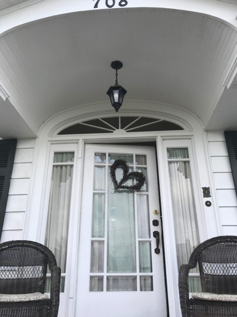 Front door of a white home with a heart-shaped wreath hanging on it.