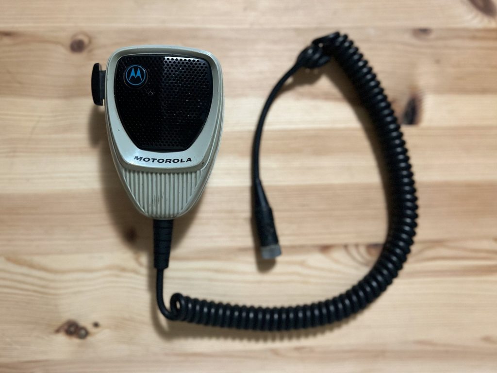 Motorola hand held radio with black coil cord on wood table
