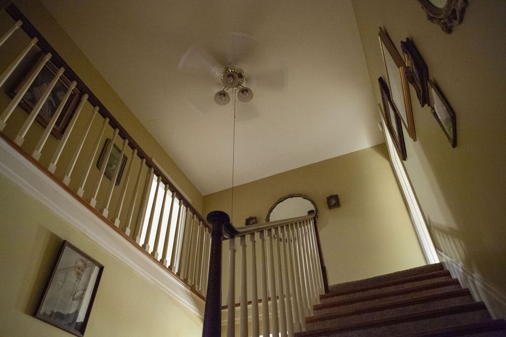 Stairs leading up to an open bedroom door with a ceiling fan spinning