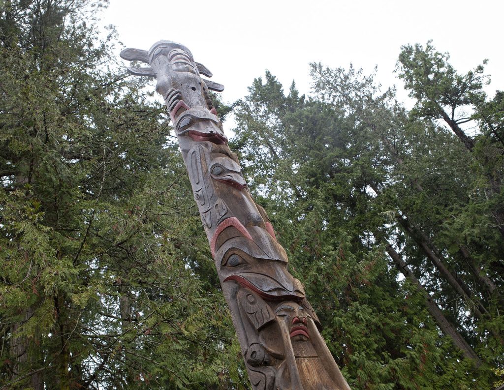 Carved wooden story pole against green fir trees