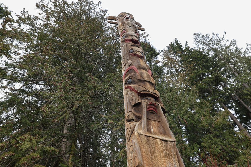 Carved wooden story pole against green fir trees