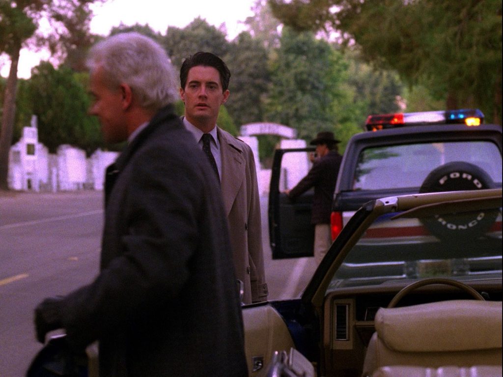 Leland Palmer and Agent Cooper standing next to Leland's car while Sheriff Truman makes a call on his police radio in his truck