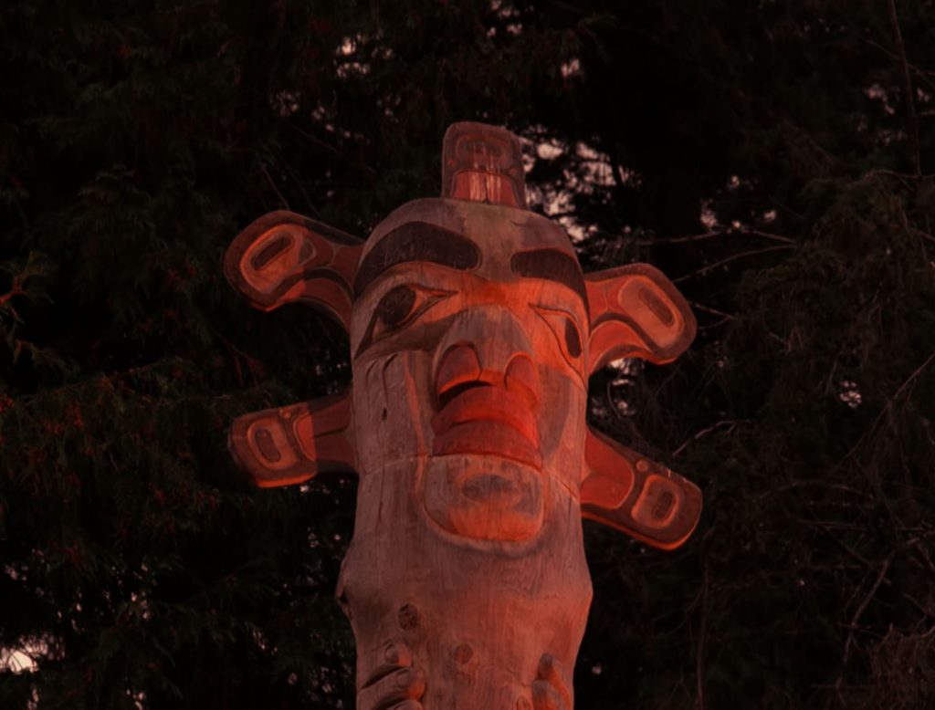 A stylized carved sun at the top of a wooden story pole
