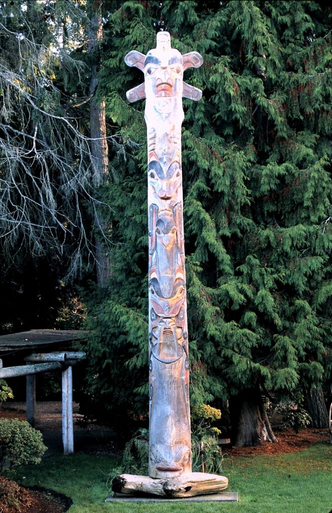 Carved wooden story pole against fir trees