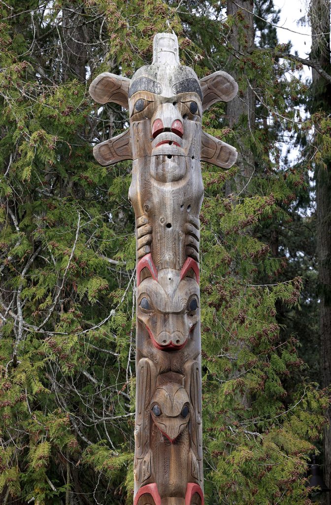 Part of a wooden carved story pole against fir trees
