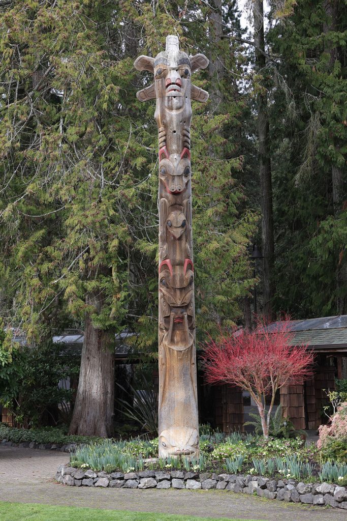 Carved wooden story pole against fir trees and along a rock-lined path