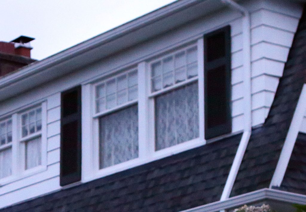 Windows with curtains on the front of a white and black house.