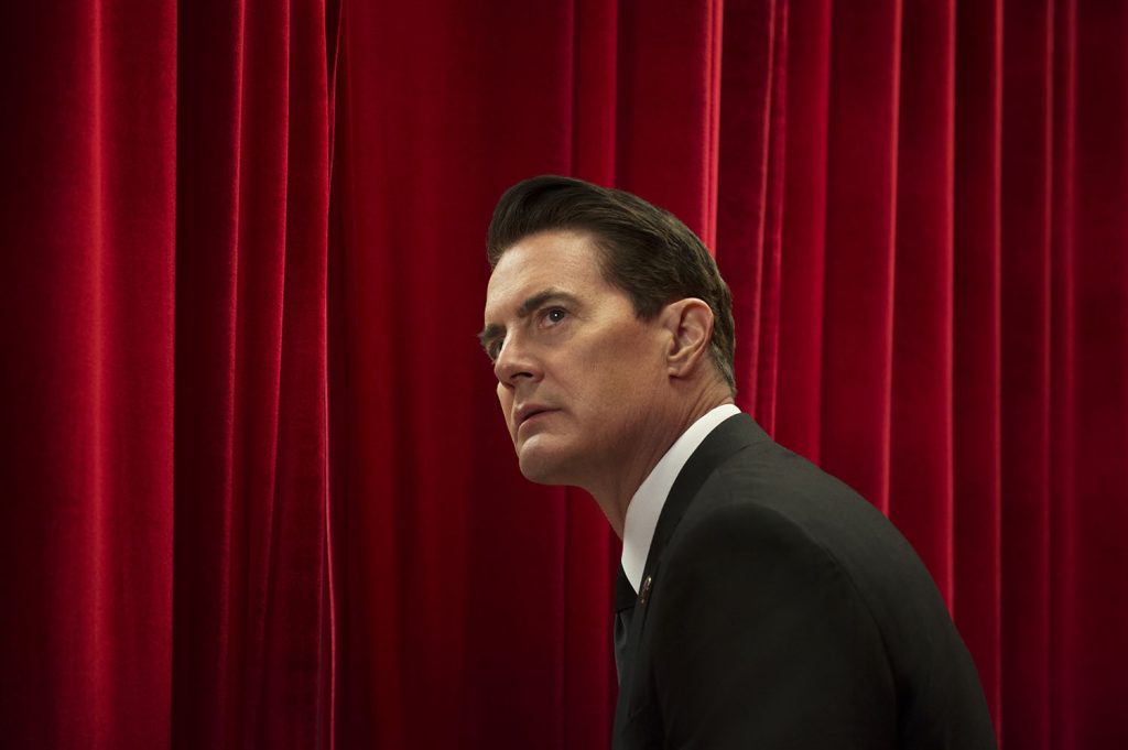 Kyle MacLachlan in a still from Twin Peaks with him dressed as Agent Cooper standing by curtains