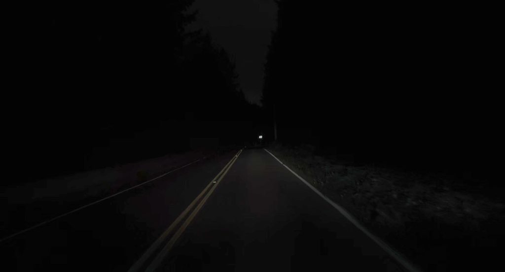 Dark two-lane road illuminated by headlights