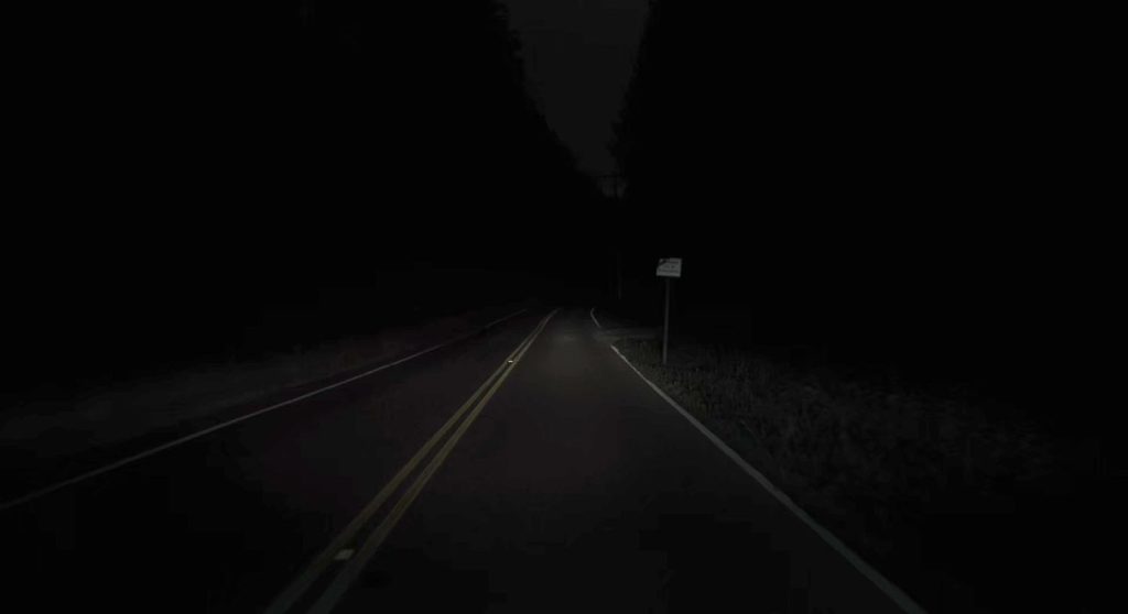 Two-lane road at night with a small street sign on the right side of the highway.