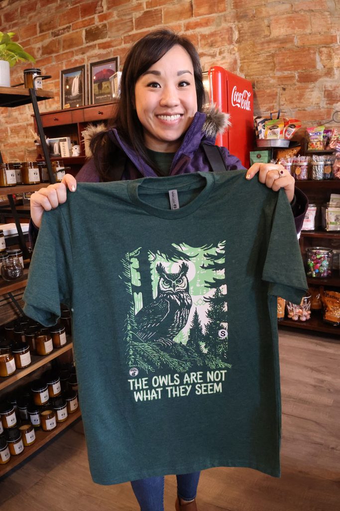 Katie holding up a t-shirt with the phrase The Owls are Not What They seem at Snoqualmie Trading Post in Snoqualmie, Washington