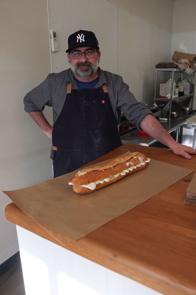 Chef Justin Fitch standing next to a table with the Best Damn Sandwich on display