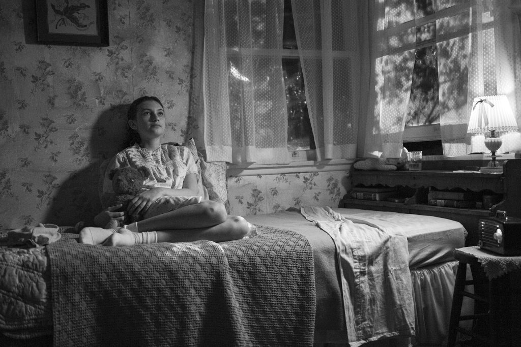 Black and white image of a girl sitting on a bed