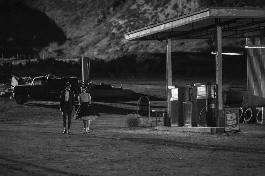 Black and White image of two people walking by a gas station