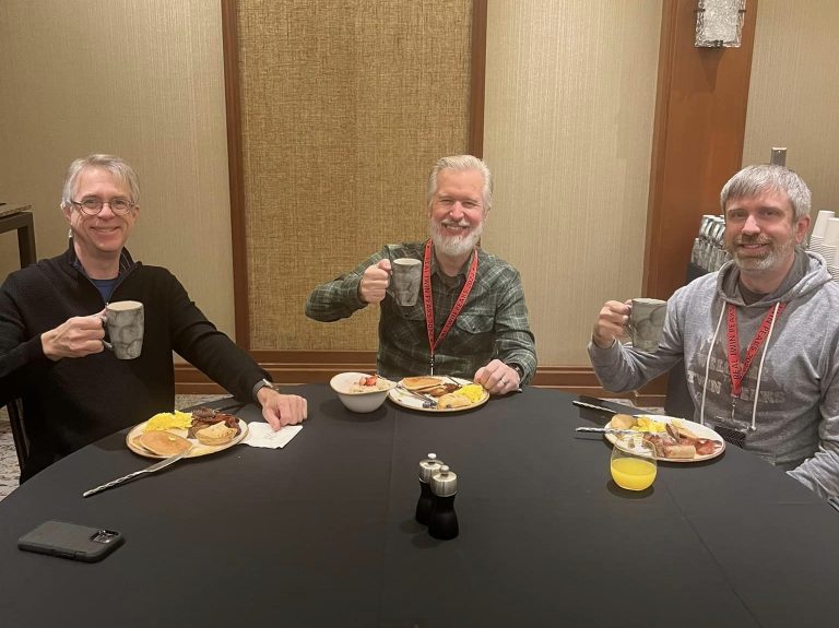 Three people at a table holding up coffee cups