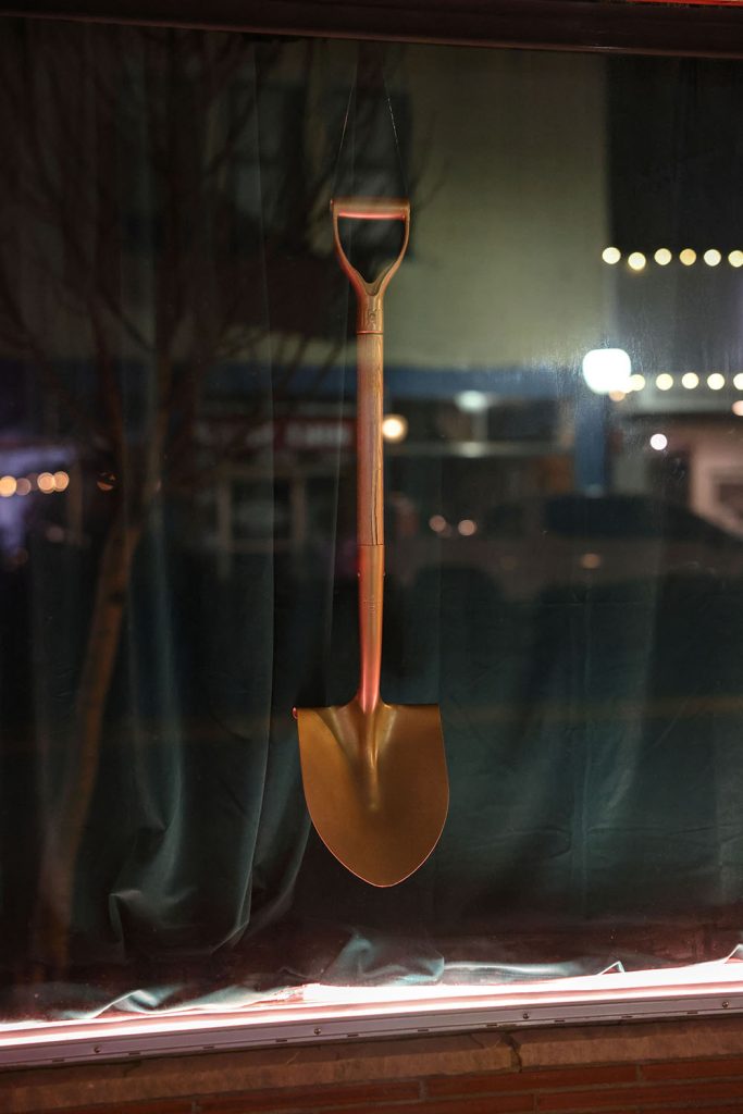 Golden shovel against green drapes in a window