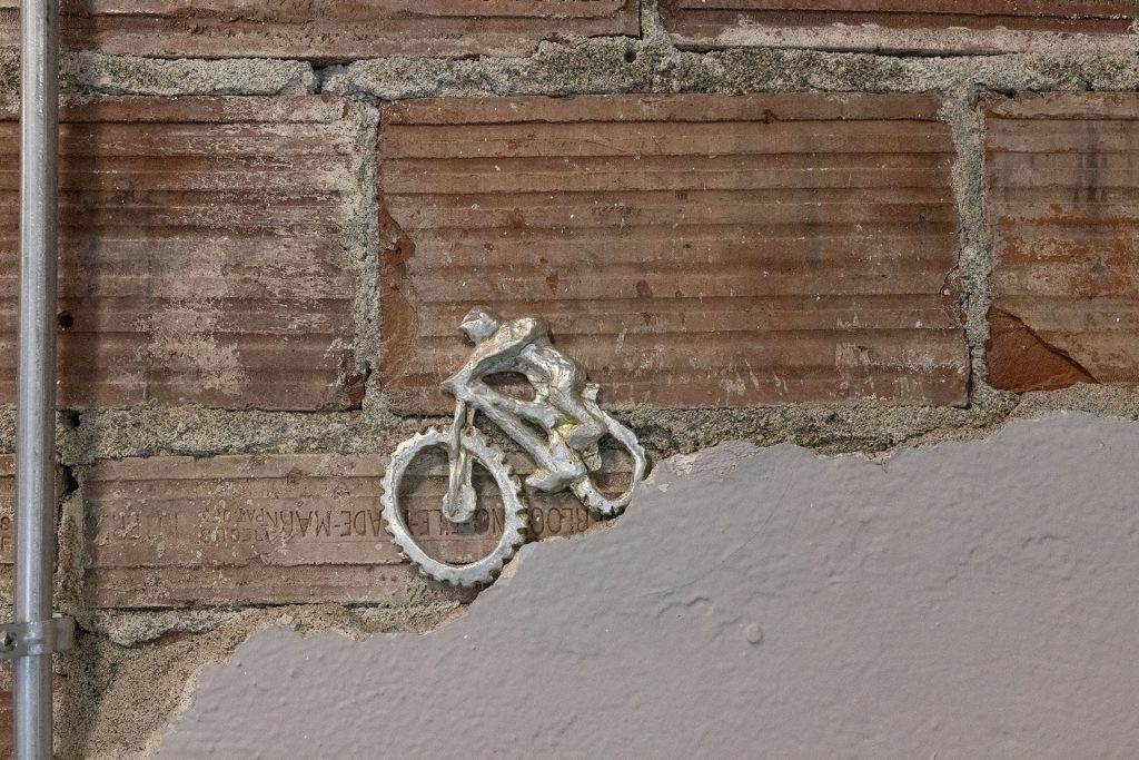 Brick wall with a tiny metal biker riding down concrete