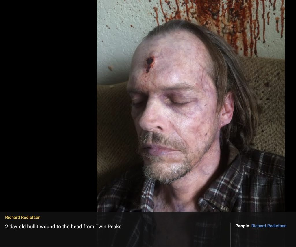 Dead guy sitting in chair with a bullet wound to the head