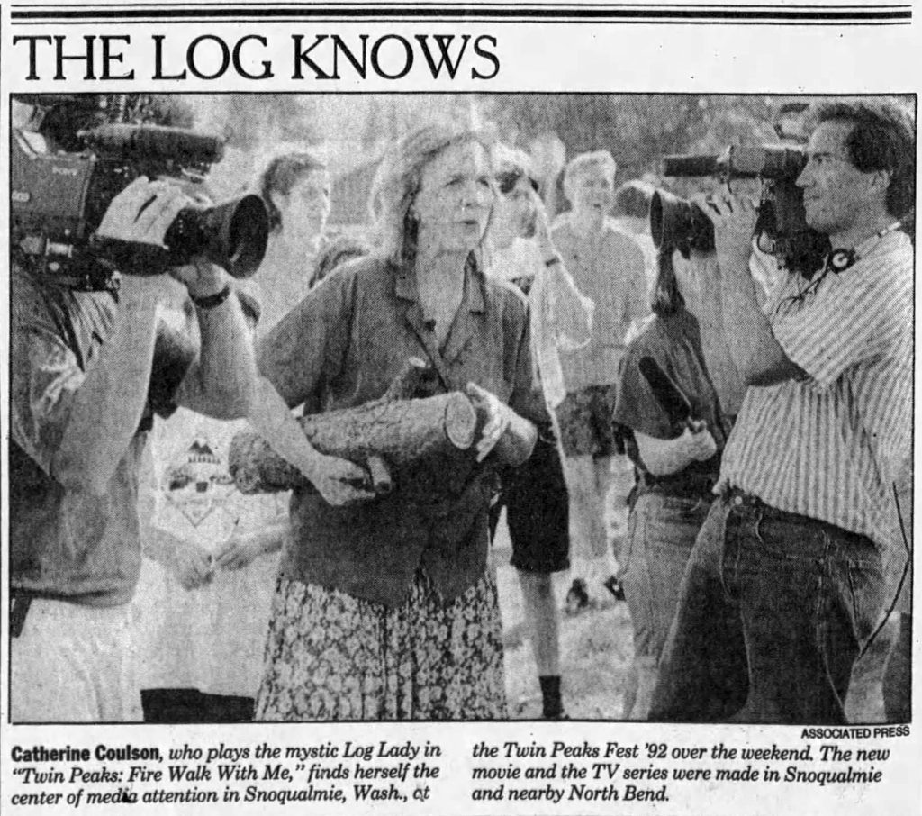 Black and white image of Catherine Coulson holding a log surrounded by reporters