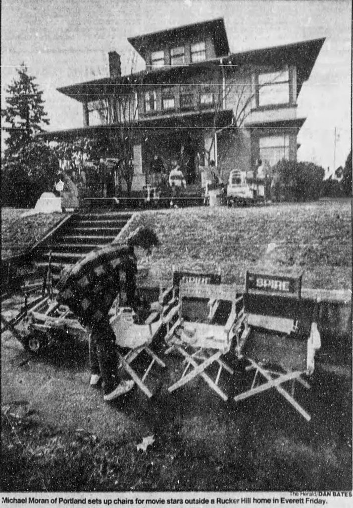 Black and white image of a home on a hill with someone setting up chairs on the sidewalk