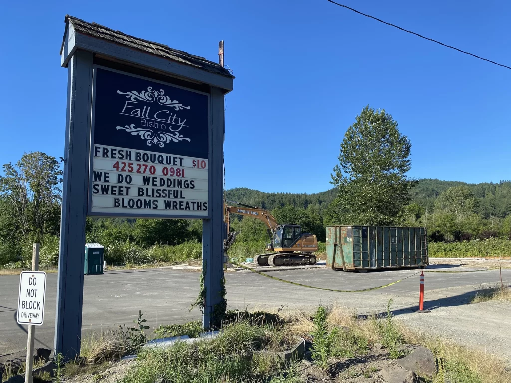 Roadside sign and empty slab with construction equipment and dumpster