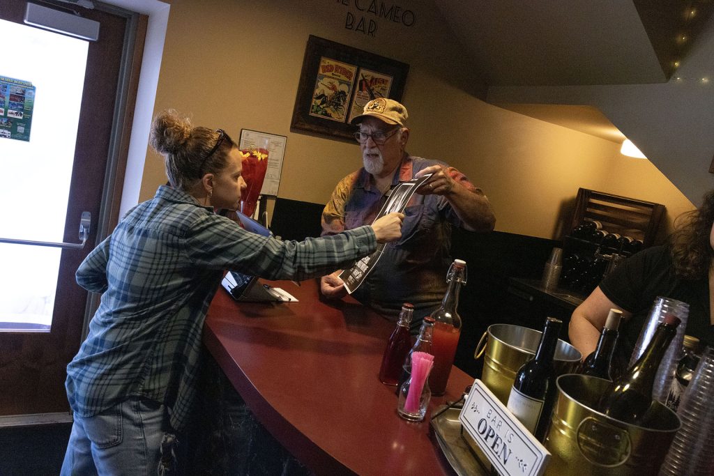 Person showing a poster to someone at a bar