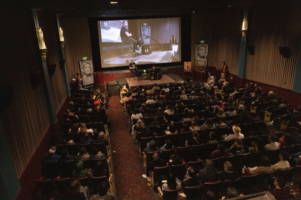 Aerial view of packed theatre with Sheryl Lee on stage