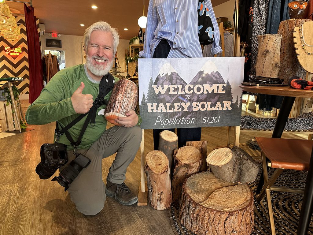 Steven kneeling with a thumbs up next to a hand drawn sign