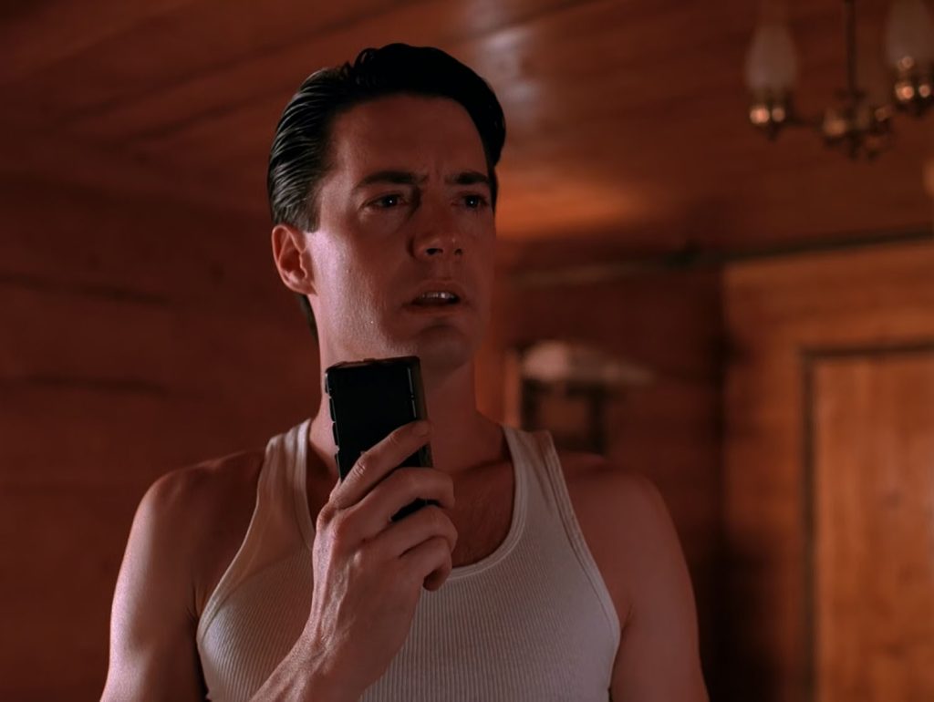 Special Agent Dale Cooper standing in his hotel room holding a tape recorder