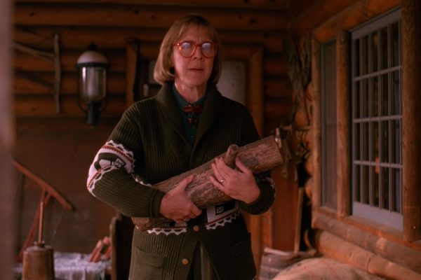 The Log Lady carrying the log as she stands on the porch