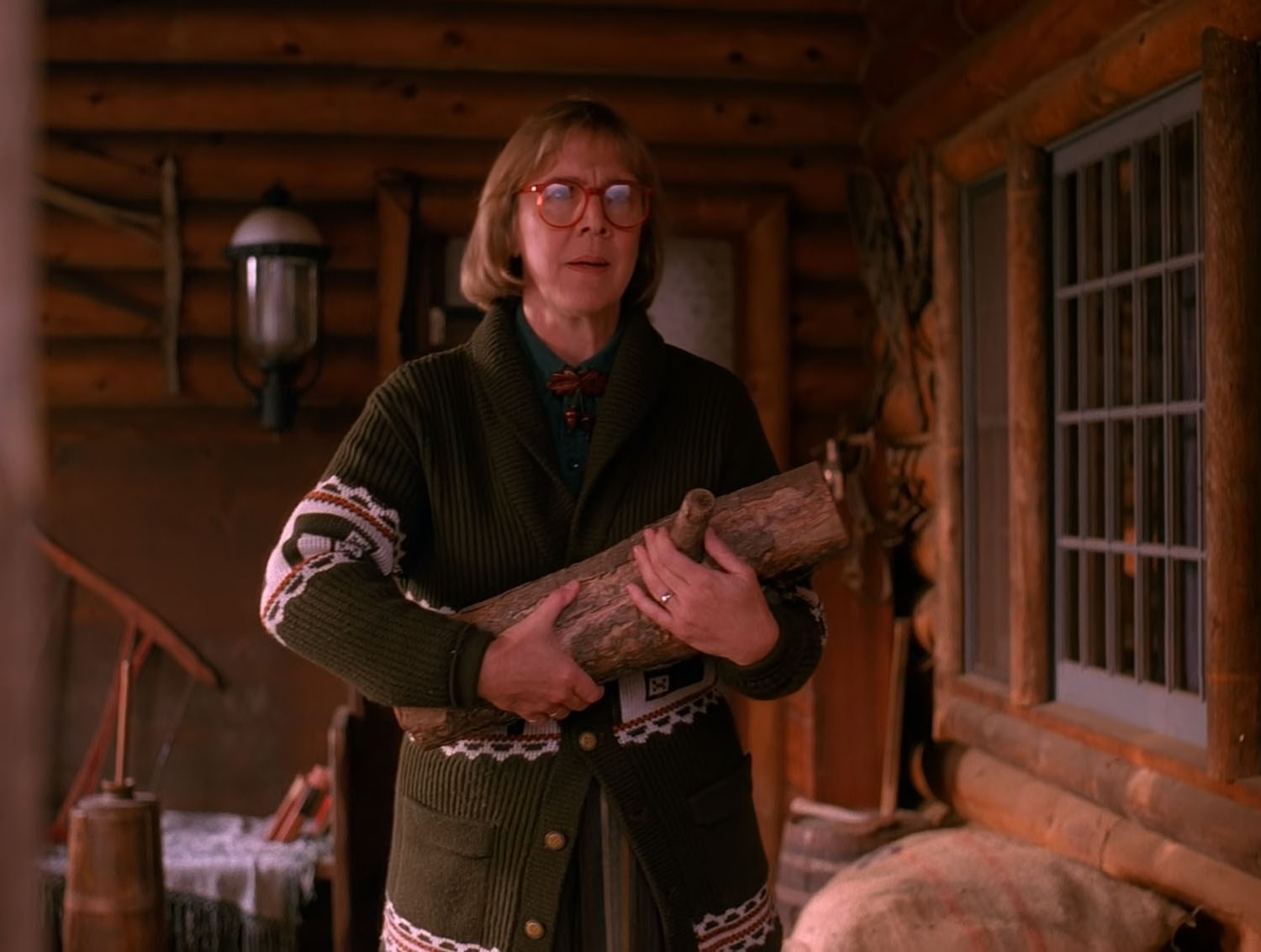 The Log Lady carrying the log as she stands on the porch