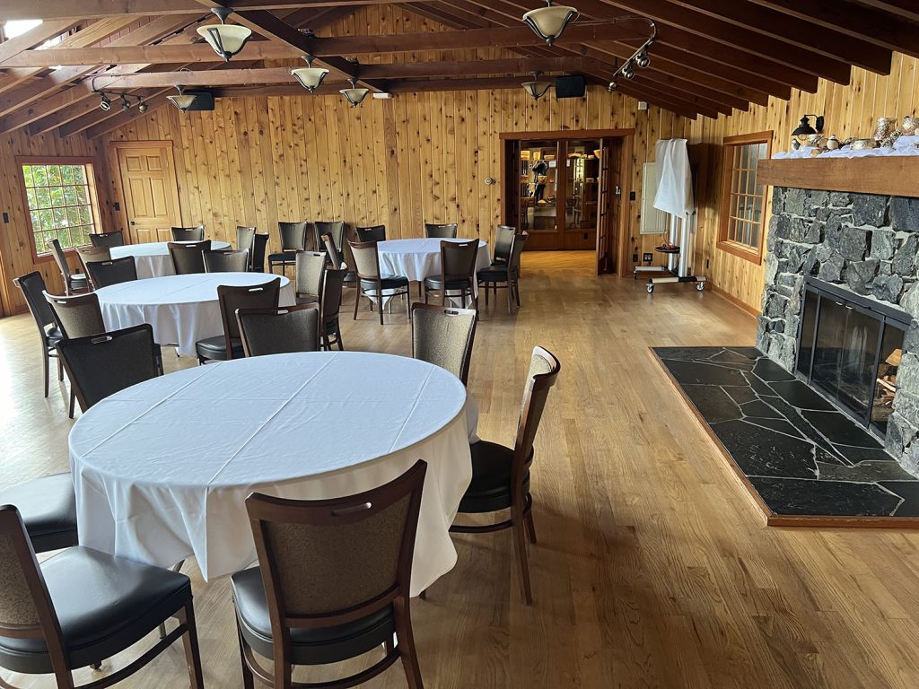 A dining room full of round tables with white linens and surrounded by chairs