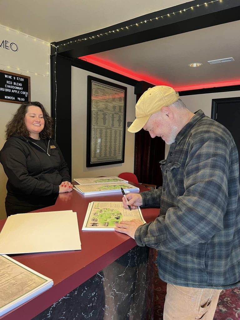 Artist Todd Gamble signing posters with Britni Larson looking on