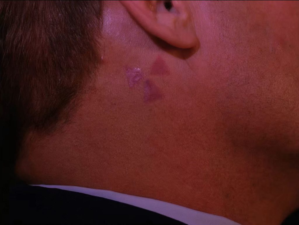 Close-up of Major Briggs' neck with three triangle tattoo