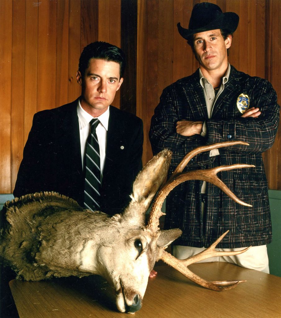 Agent Cooper and Sheriff Truman standing over a deer head on a table