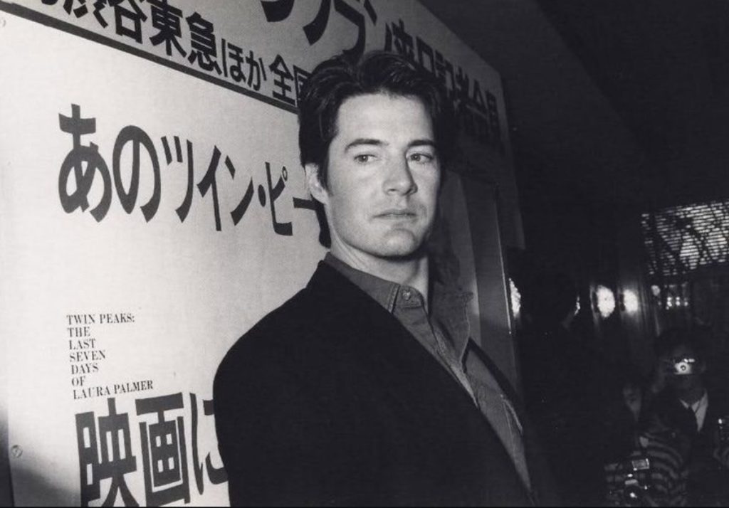 Black and white photo of Kyle MacLachlan in front of a banner