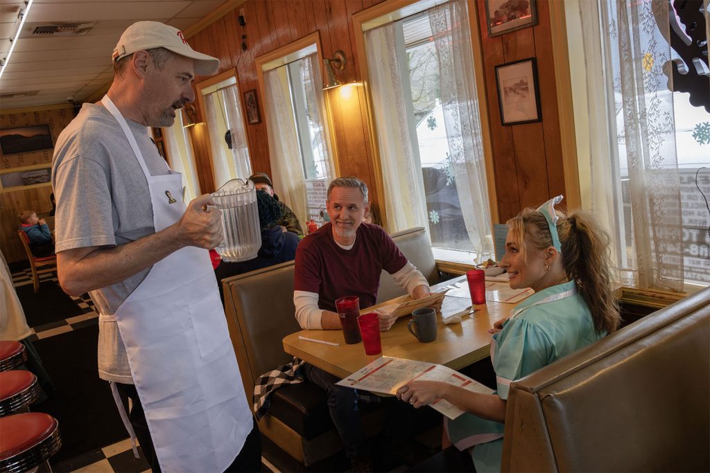 Scott Ryan serving water to two guests dressed as Bobby Briggs and Shelly Johnson