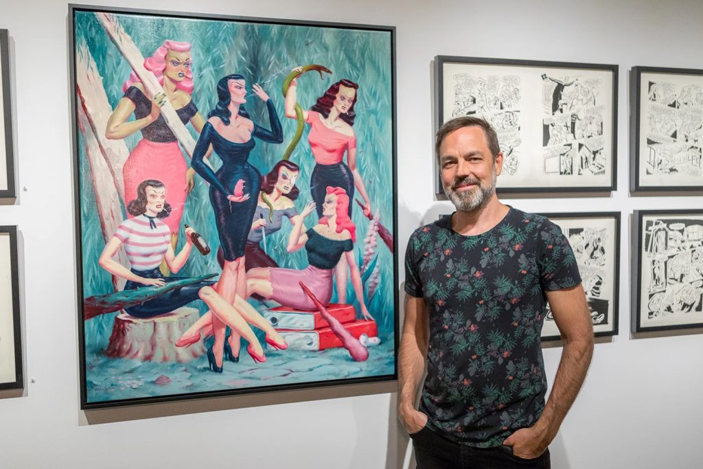 Ryan Heshka standing by artwork in a gallery
