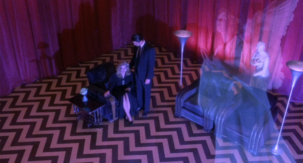 Laura Palmer sitting in the Red Room with Agent Cooper standing nearby and an angel floating above the space
