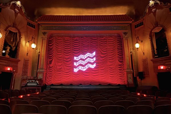 Inside of a movie theatre with seats and a red curtain