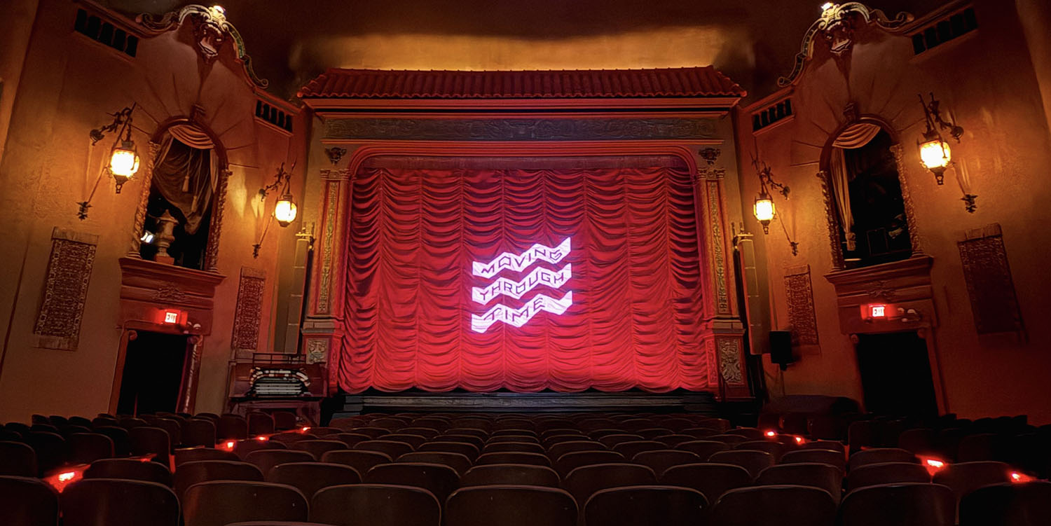 Inside of a movie theatre with seats and a red curtain