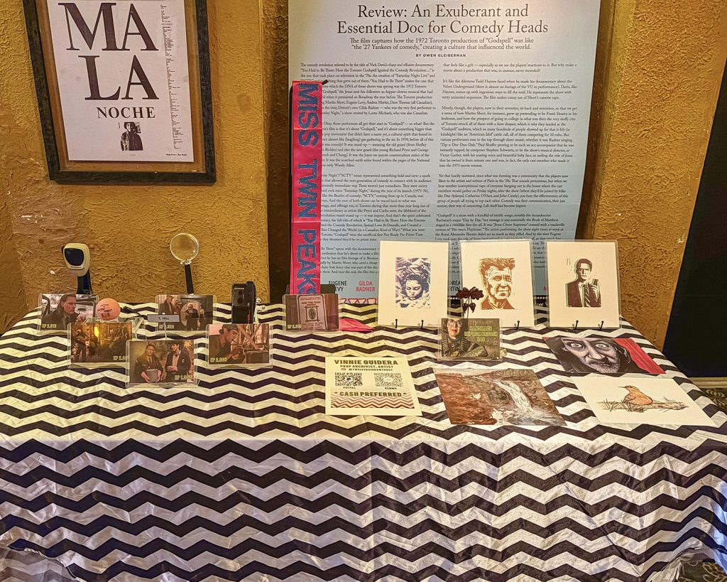 Table with a black and white chevron pattern table cloth adorned with Twin Peaks props and artwork